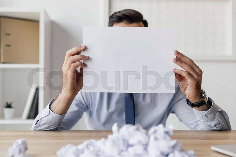 Obscured view of businessman covering face with blank paper in hands, stock photo