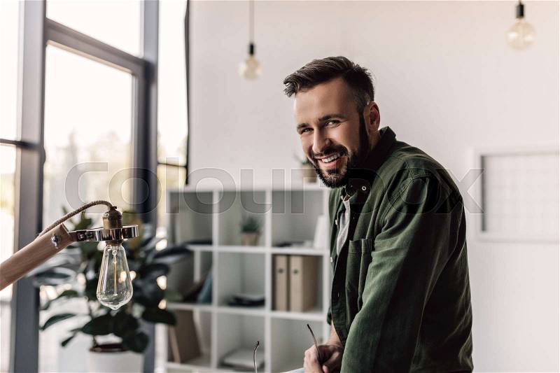 Bearded businessman in casual clothing smiling at camera in modern office, stock photo