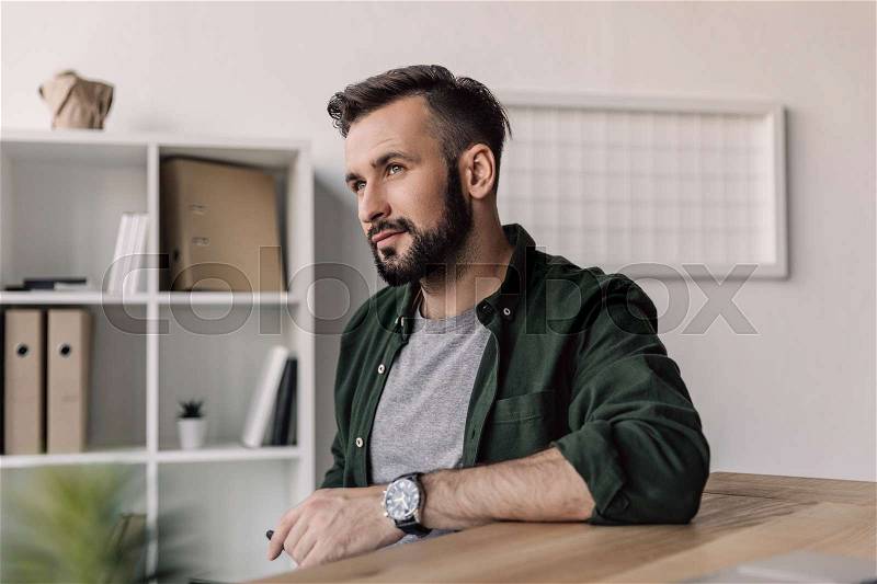 Pensive smiling bearded businessman looking away in modern office, stock photo