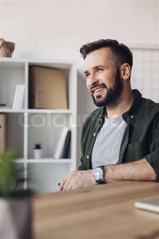 Handsome bearded man smiling and looking away in office, stock photo