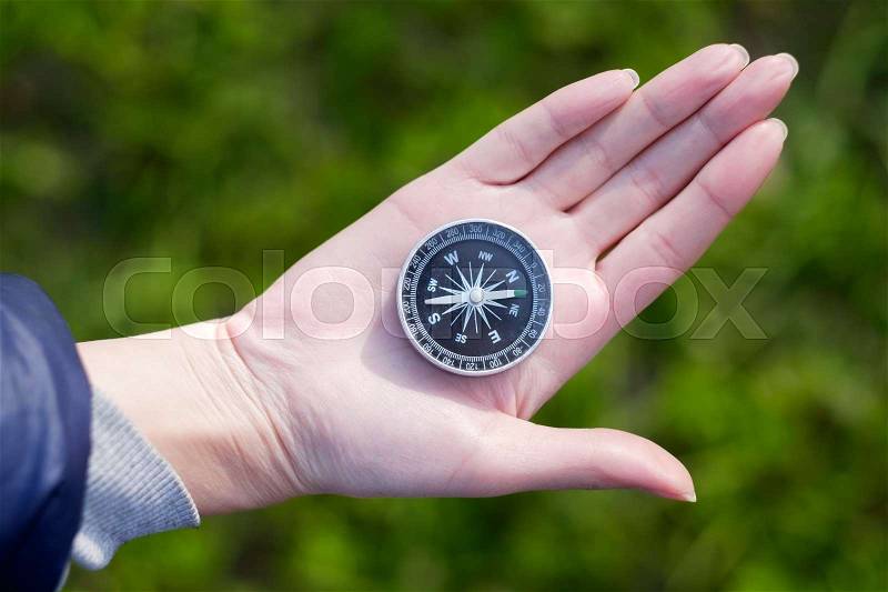 Hand holding the black compass isolated on green background, stock photo