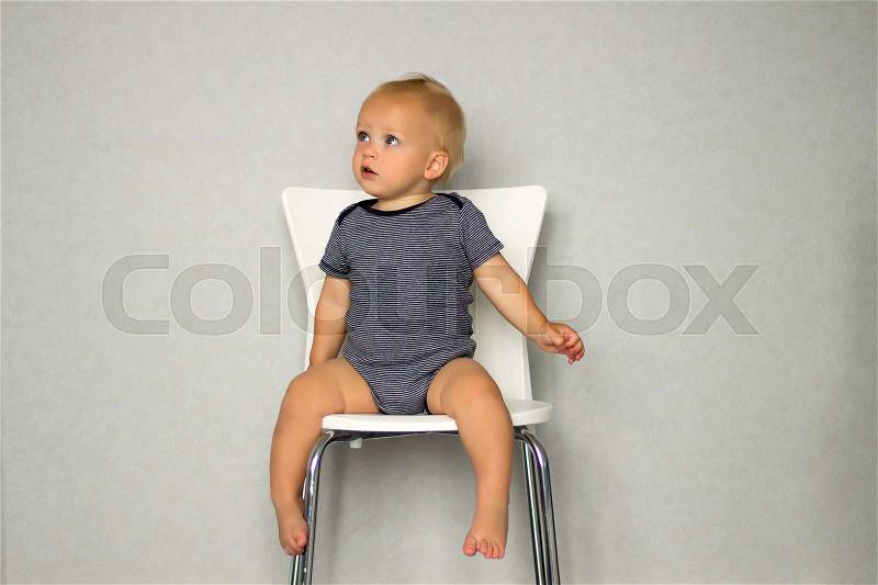 Thoughtful baby boy sitting on the chair iand looking away, stock photo
