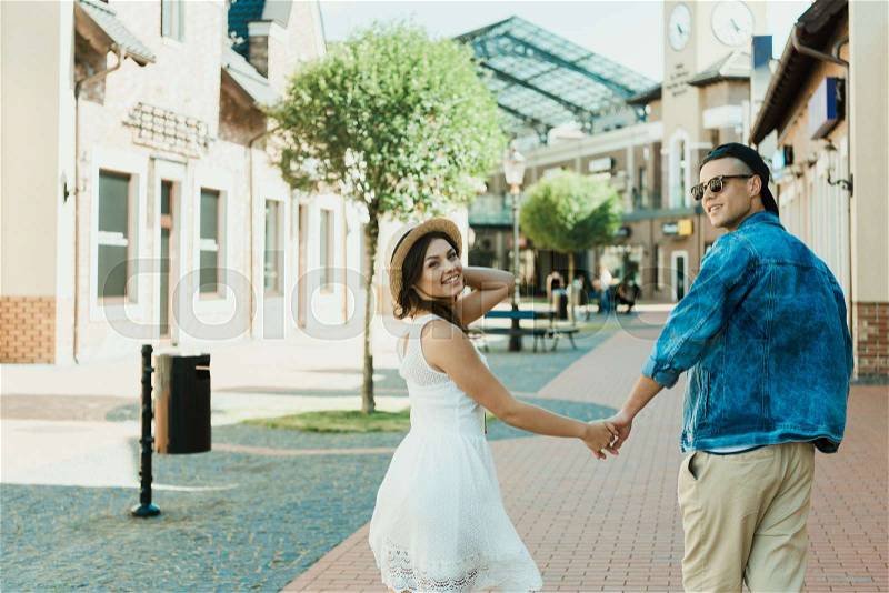 Smiling trendy couple holding hands while walking in city, stock photo
