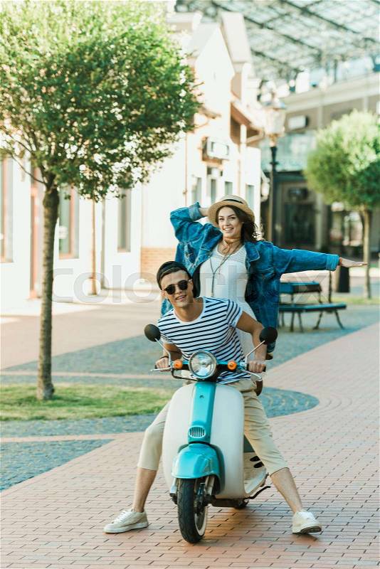 Happy stylish young couple riding scooter and smiling at camera , stock photo