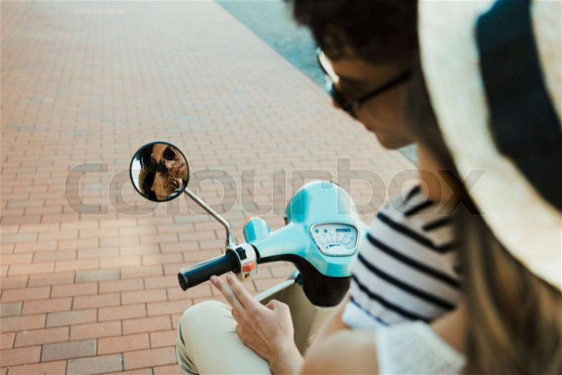 Cropped shot of young couple riding scooter and looking at reflection in mirror, stock photo