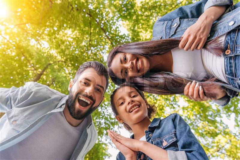 Bottom view of happy young family standing together and smiling at camera in park, stock photo