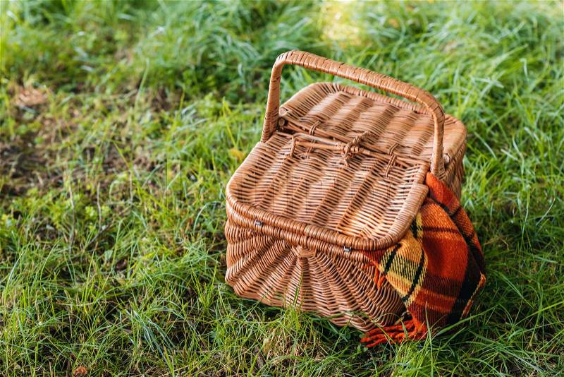 Top view of wicker picnic basket with rug on green grass , stock photo