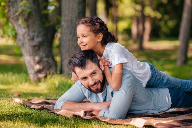 Portrait of little girl lying on fathers back while spending time together, stock photo