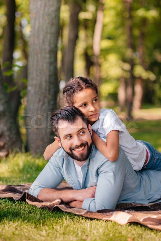 Portrait of little girl lying on fathers back while spending time together outdoors, stock photo