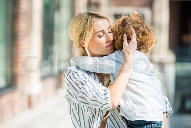 Portrait of sensual mother with eyes closed hugging little son, stock photo