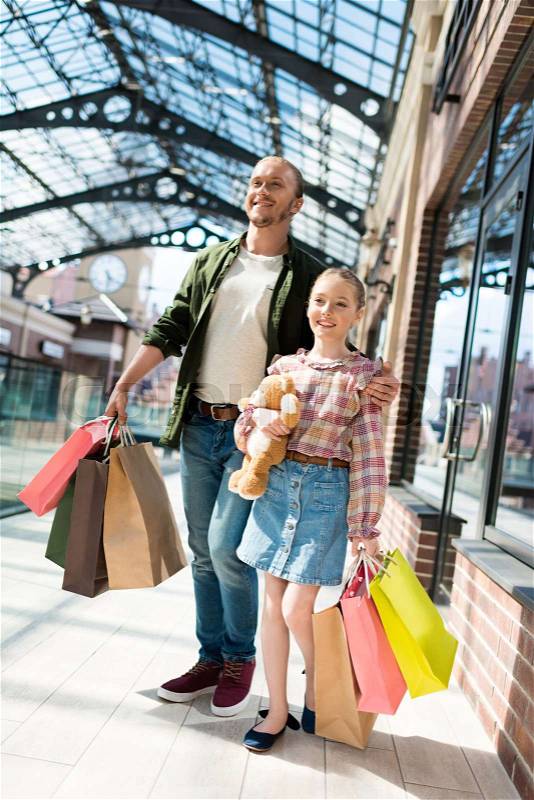 Father and daughter holding shopping bags while walking in shopping mall, stock photo