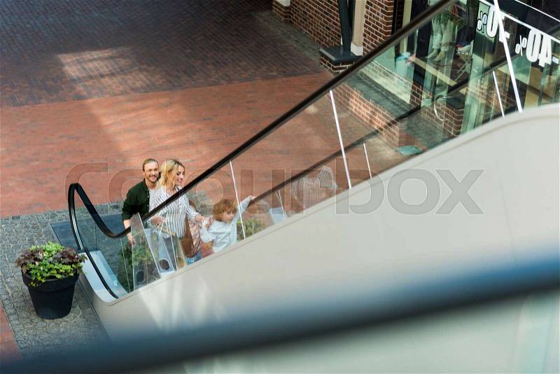 High angle view of happy parents with cute little son standing on escalator in shopping mall, stock photo