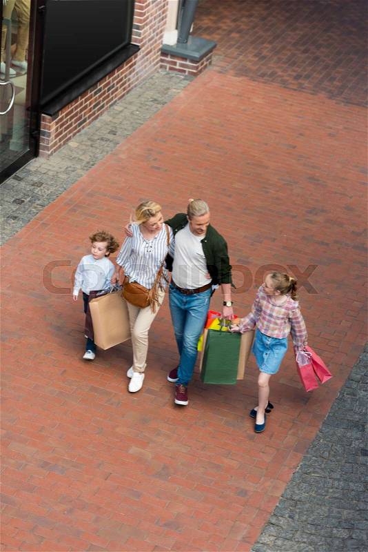 High angle view of happy family with two children holding paper bags and walking together, stock photo