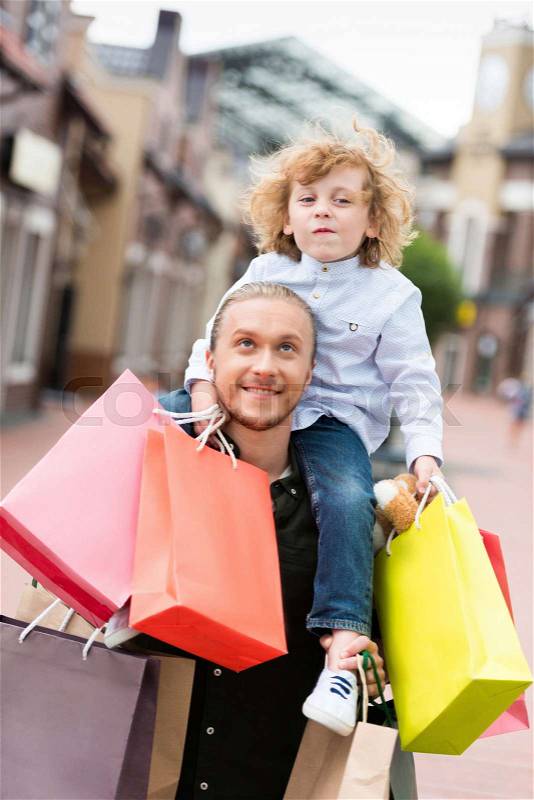 Portrait of smiling father piggybacking his little son with shopping bags at street , stock photo