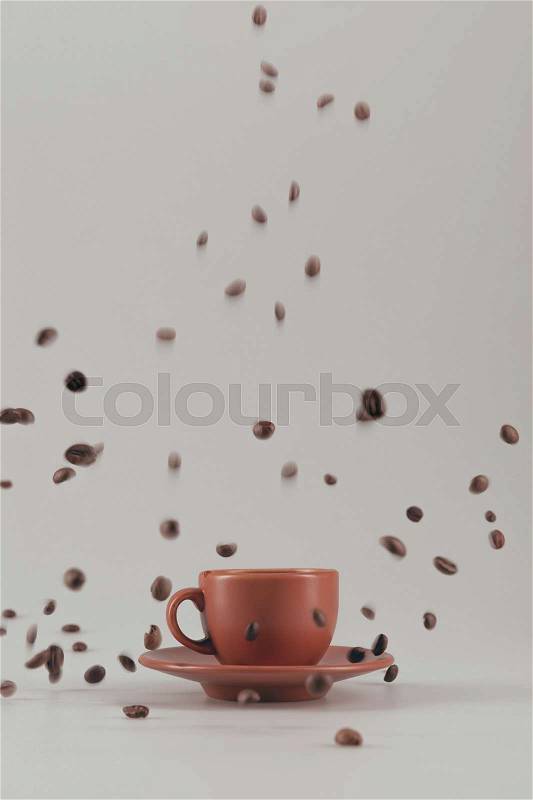 Ceramic coffee cup with falling coffee grains isolated on grey, stock photo