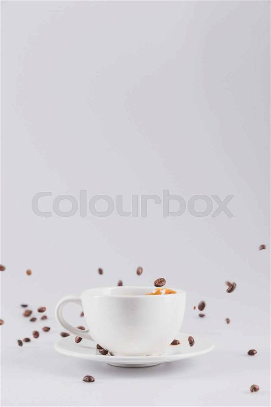 White coffee cup on saucer with scattered coffee grains isolated on grey with copy space, stock photo