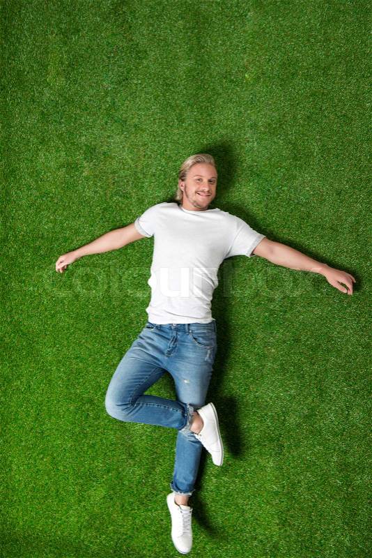 Above view of young caucasian man relaxing and lying on meadow, stock photo