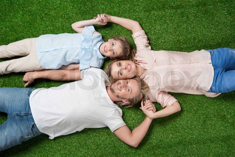 Above view of happy family looking at camera while lying on the grass, stock photo