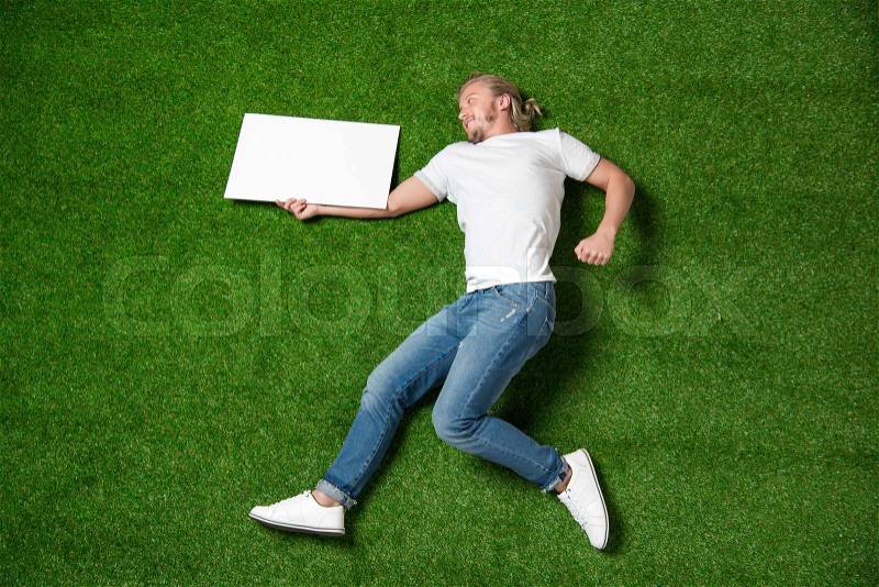 Above view of young man holding blank placard while lying on meadow, stock photo