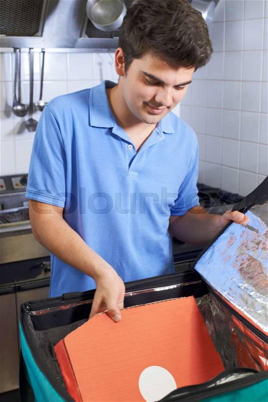 Pizza Delivery Person Putting Food Into Insulated Bag In Restaurant Kitchen, stock photo