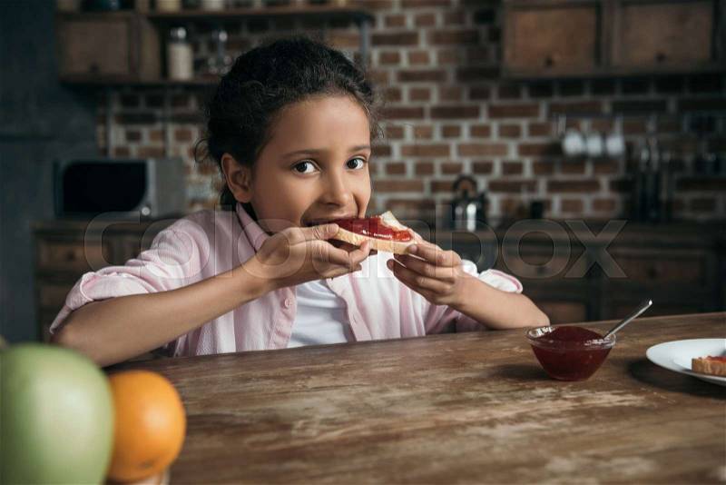 Little girl eating toast with homemade jam at home, stock photo