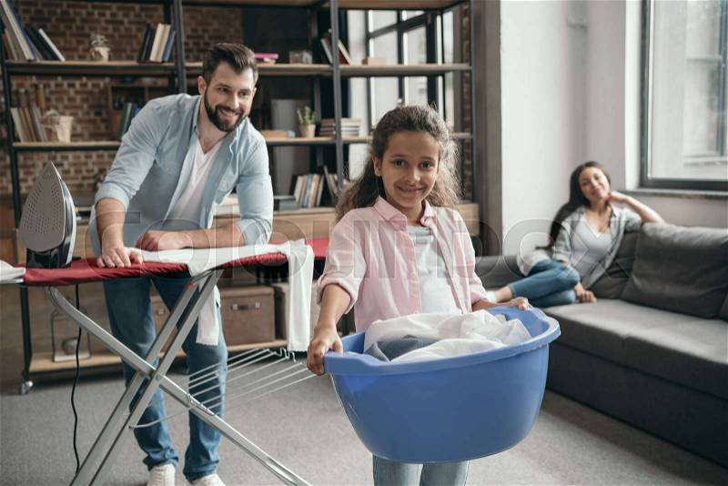 Happy casual multiethnic family ironing clothes at home, stock photo
