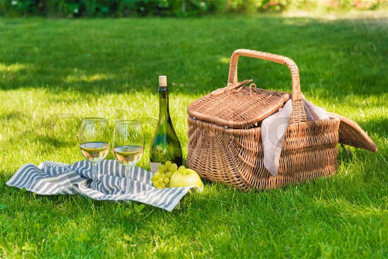 Close-up view of wicker picnic basket, fruits and bottle of wine with glasses on napkin, stock photo