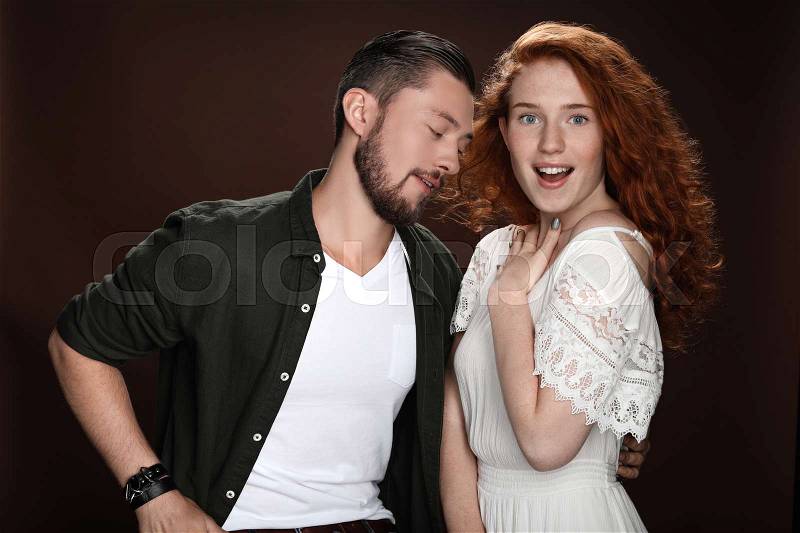 Sensual man looking at shocked redhead woman, isolated on brown, stock photo