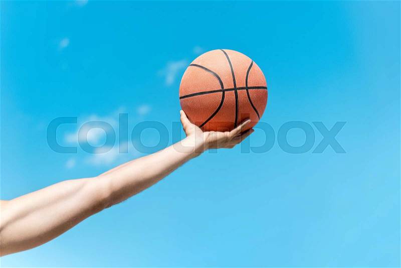 Cropped shot of hand holding basketball ball against clear blue sky, stock photo