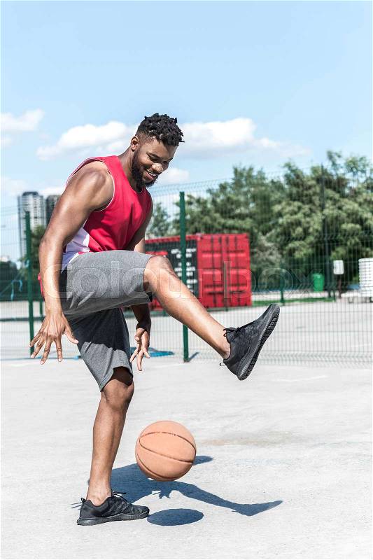 Cheerful basketball player training with basketball ball at court, stock photo