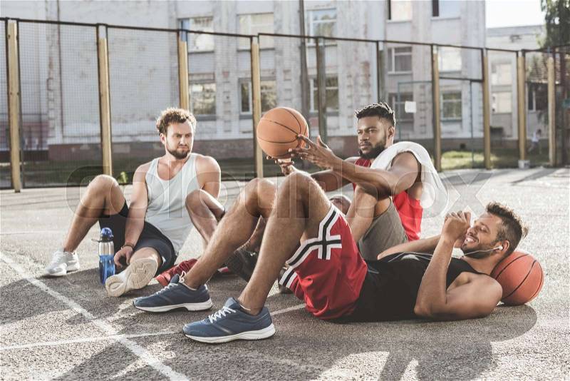 Multiethnic group of men resting after basketball game on court, stock photo