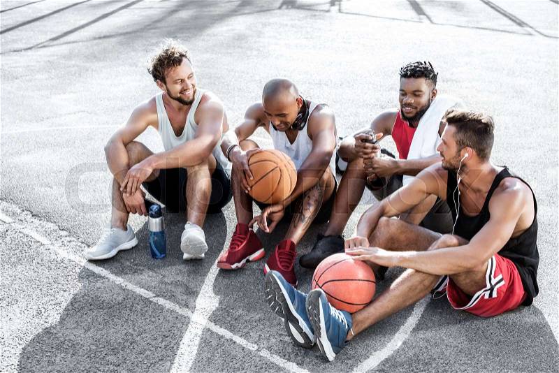 Multiethnic group of basketball players resting on court together, stock photo