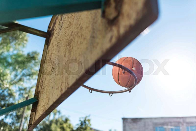 Close up view of basketball ball falling into basket against blue sky, stock photo