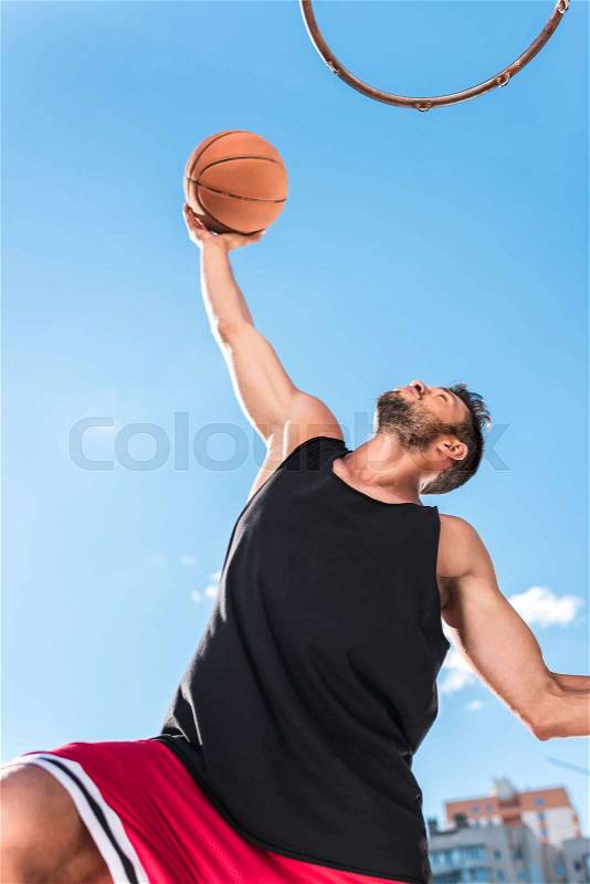 Low angle view of basketball player throwing ball into basket, stock photo