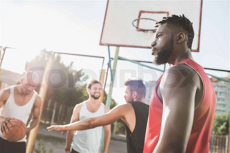 Group of young multicultural men playing basketball on court, stock photo