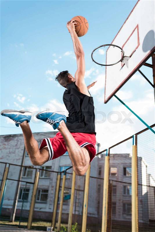 Back view of basketball player throwing ball into basket during game, stock photo