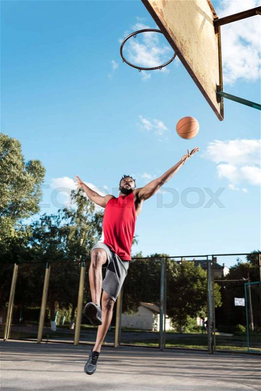 African american basketball player throwing ball into basket during game, stock photo