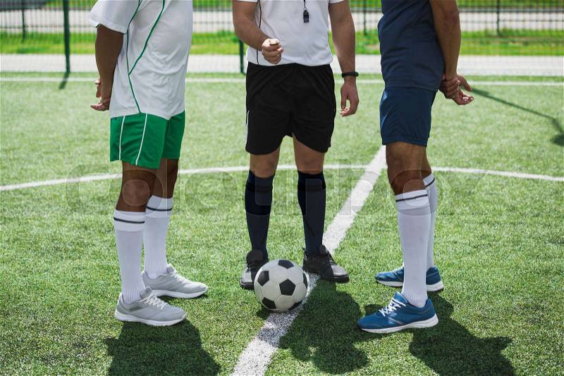 Cropped shot of referee and soccer players on soccer pitch starting game, stock photo