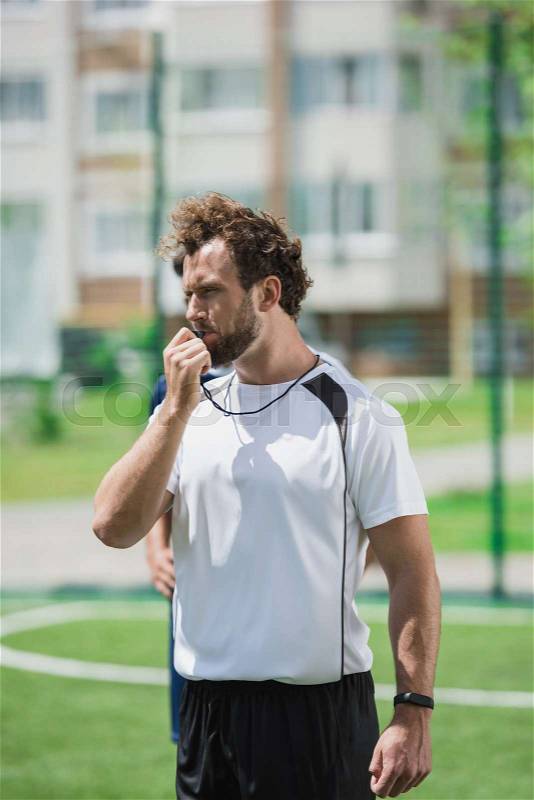Portrait of soccer referee whistling in whistle on soccer pitch during game, stock photo