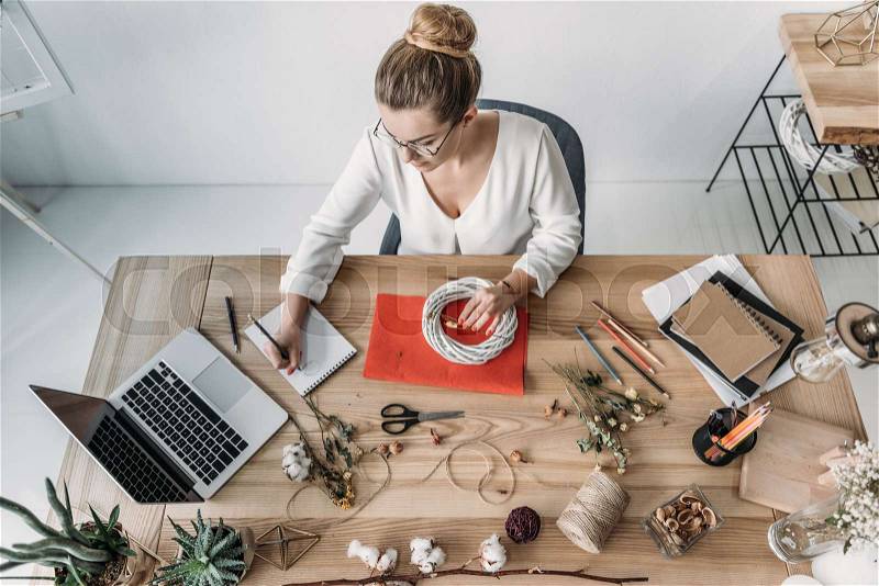 Top view of blonde female florist working with laptop and dry flowers at workplace, stock photo