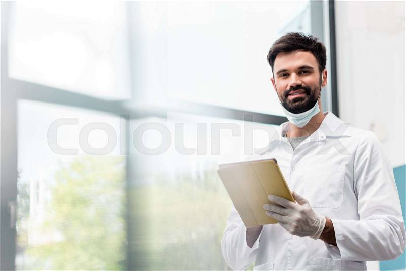Bearded male scientist in lab coat using digital tablet and smiling at camera, stock photo
