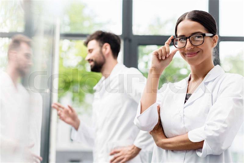 Team of professional scientists in white coats smiling while standing in laboratory, stock photo