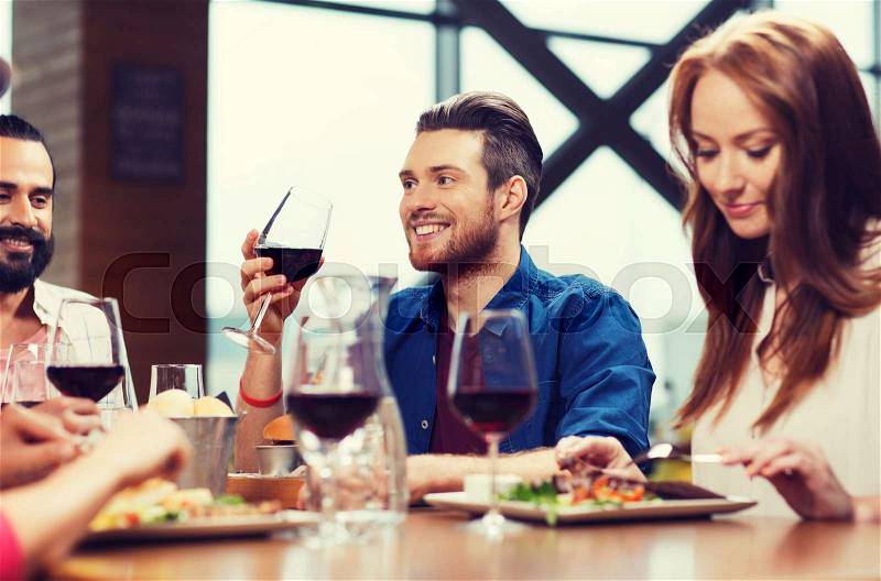 Leisure, eating, food and drinks, people and holidays concept - smiling friends having dinner and drinking red wine at restaurant, stock photo