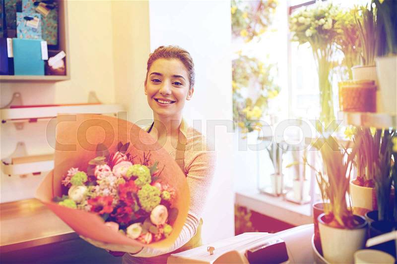 People, business, sale and floristry concept - happy smiling florist woman holding bunch of flowers wrapped into paper at flower shop, stock photo