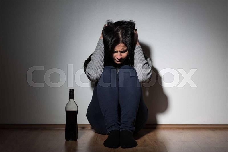 Alcoholism, depression and people concept - unhappy woman with bottle of alcohol crying at home, stock photo