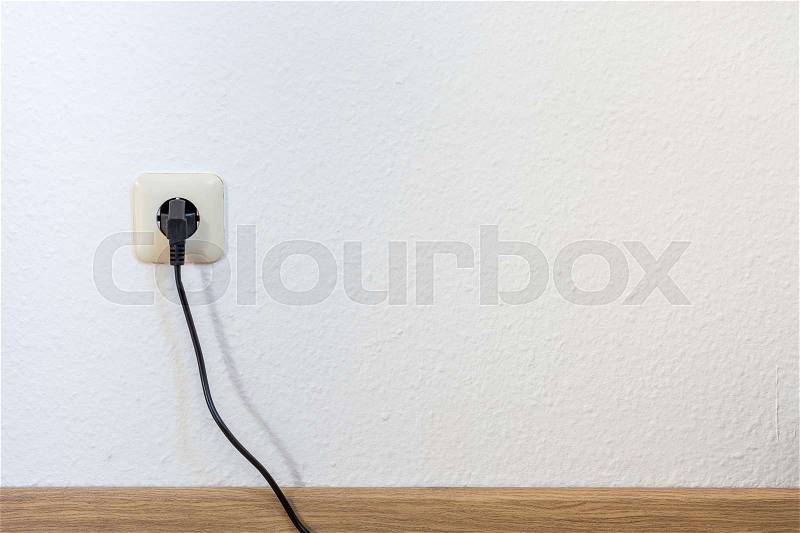 One single european plug with black cable on a white wall from the front, stock photo