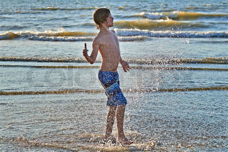 Young boy enjoying to play with water on the beach, stock photo