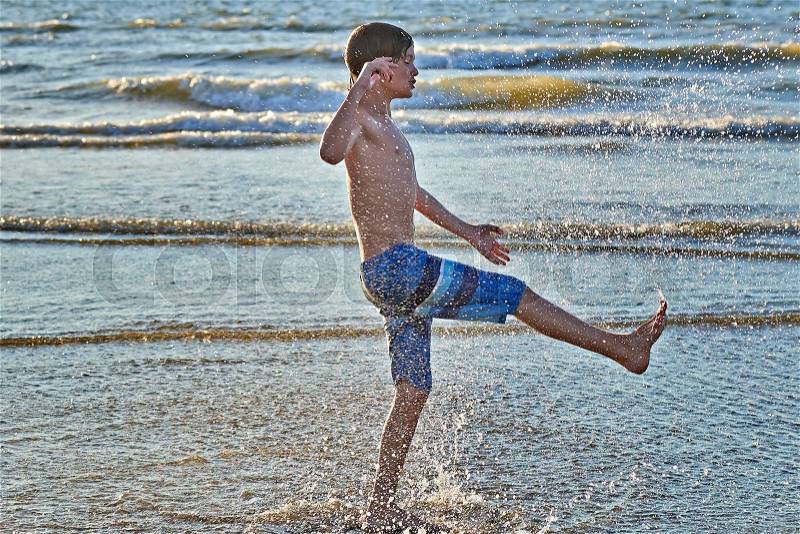 Young boy enjoying to play with water on the beach, stock photo