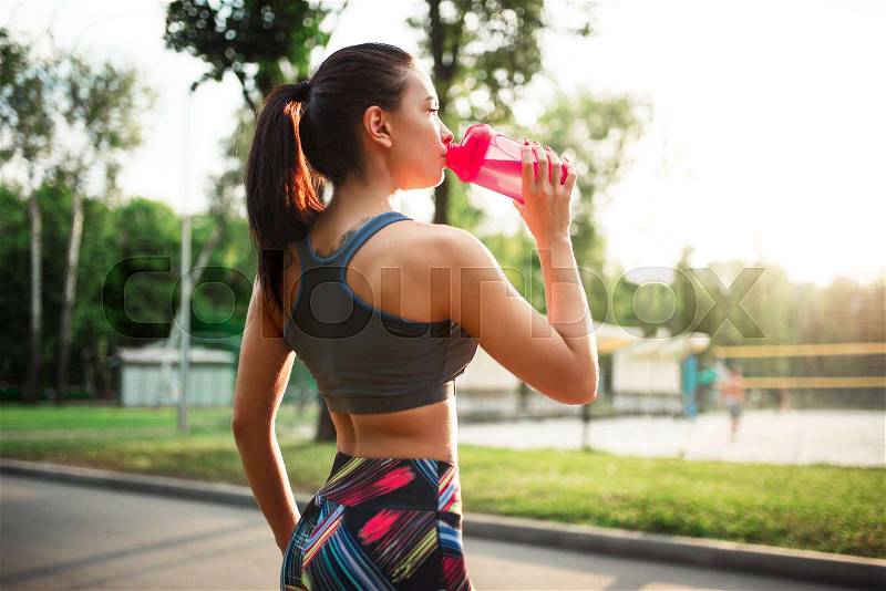Sporty woman drink water from sport bottle, training in summer park. Girl on outdoors workout, stock photo
