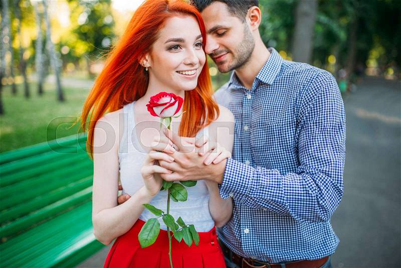 Love couple walk and hugs in summer park. Attracrive woman with rose and young man leisure together outdoors. Romantic date, stock photo